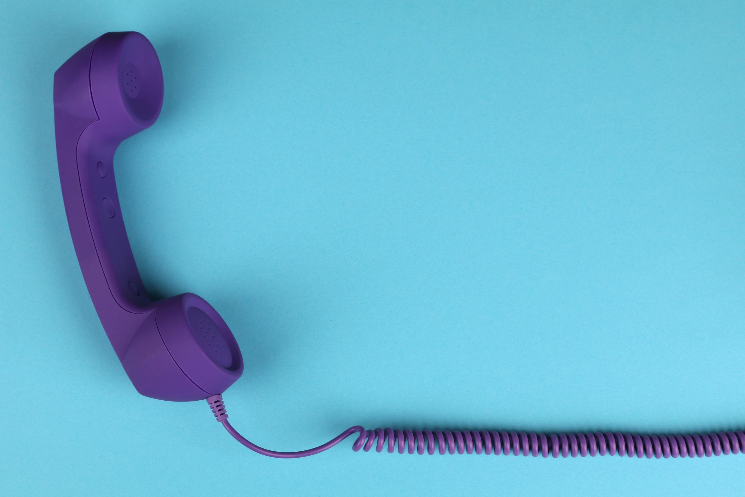 Close-up of a purple corded telephone handset on a blue background, minimalist design.