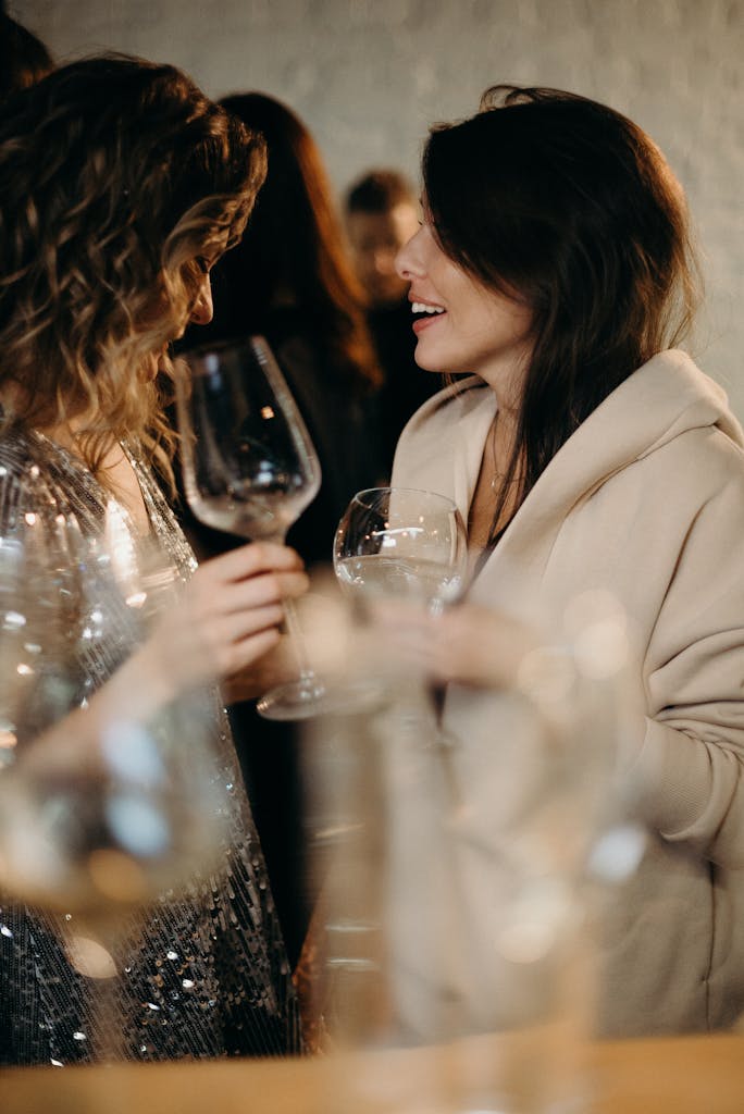 Two women enjoying a spirited conversation over wine at a lively gathering.