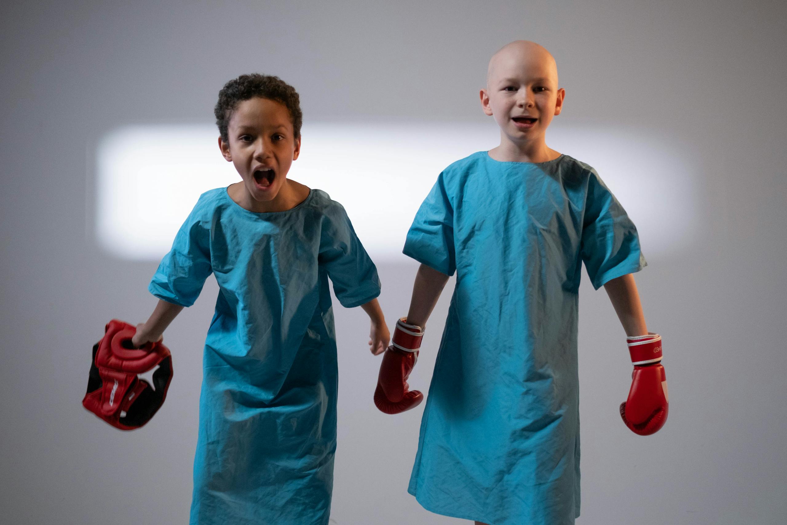 Two young boys in blue hospital gowns wearing boxing gloves, showcasing strength and resilience.